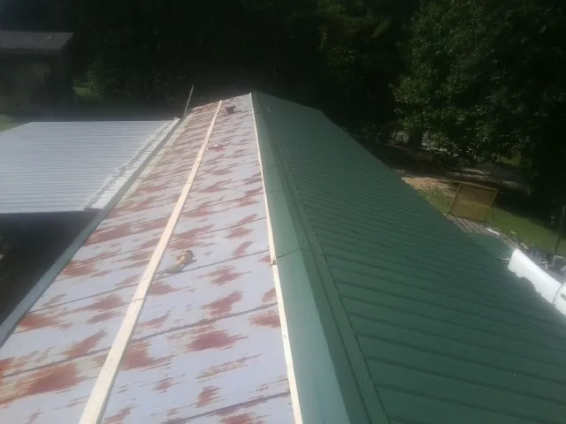Old rusted panels beside newly installed green metal roofing — Wind Damage Roof Repair by Roofing Brothers in Isle