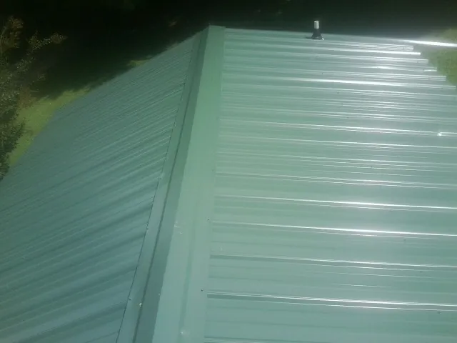 New green metal panels meeting at the ridge of a roof — Flat Roof Repair work by our crew in Isle