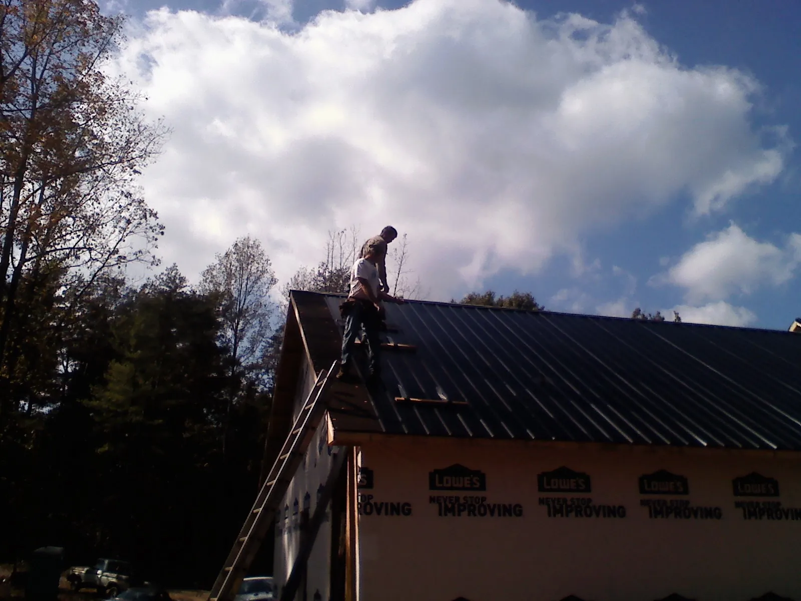 Roofer fastening dark metal panels high against a cloudy sky, from a Roof Inspection job in Isle