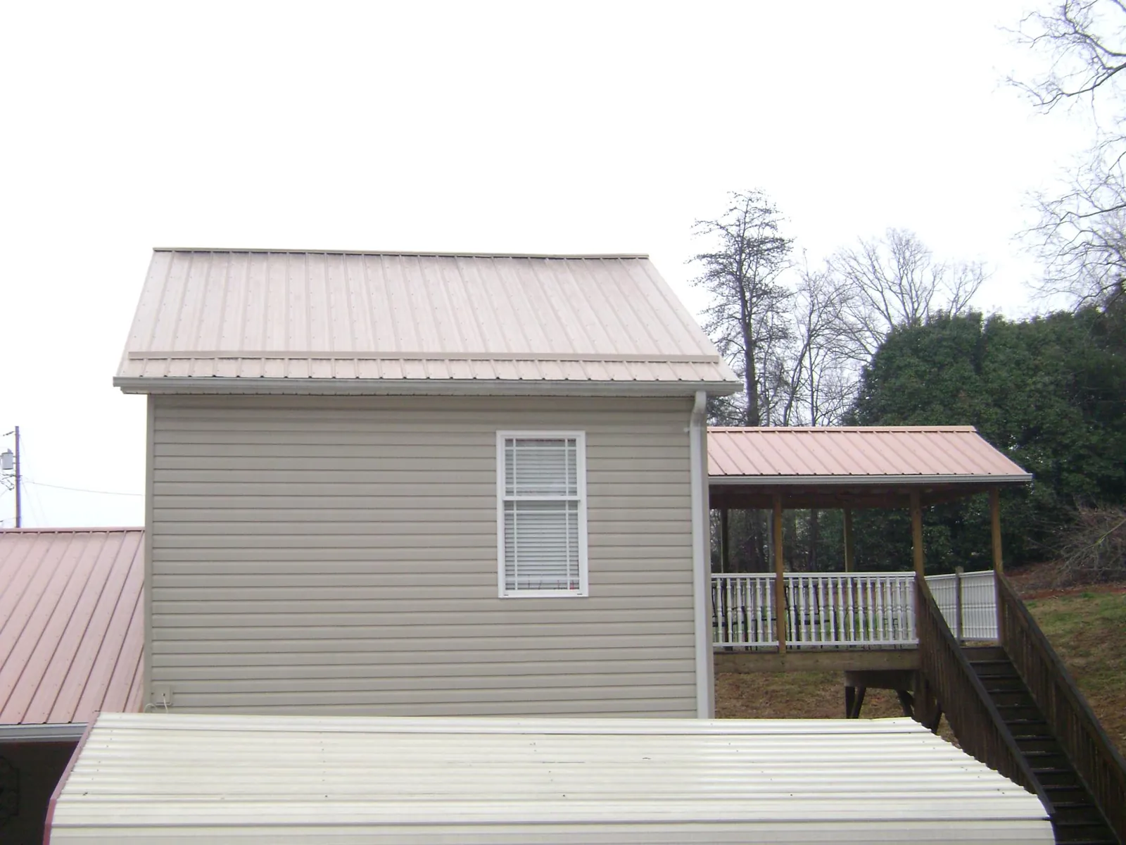 Tan metal roofs on a two story addition and attached porch, from a Roof Replacement job in Isle